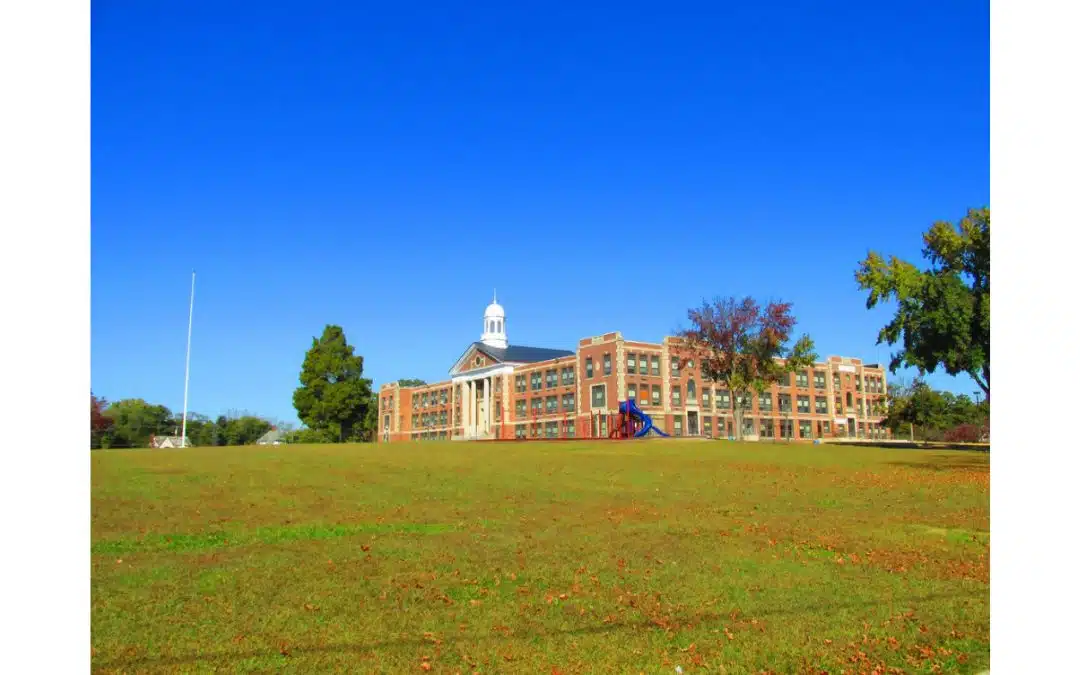 A green meadow in the foreground with a large brick school in the background